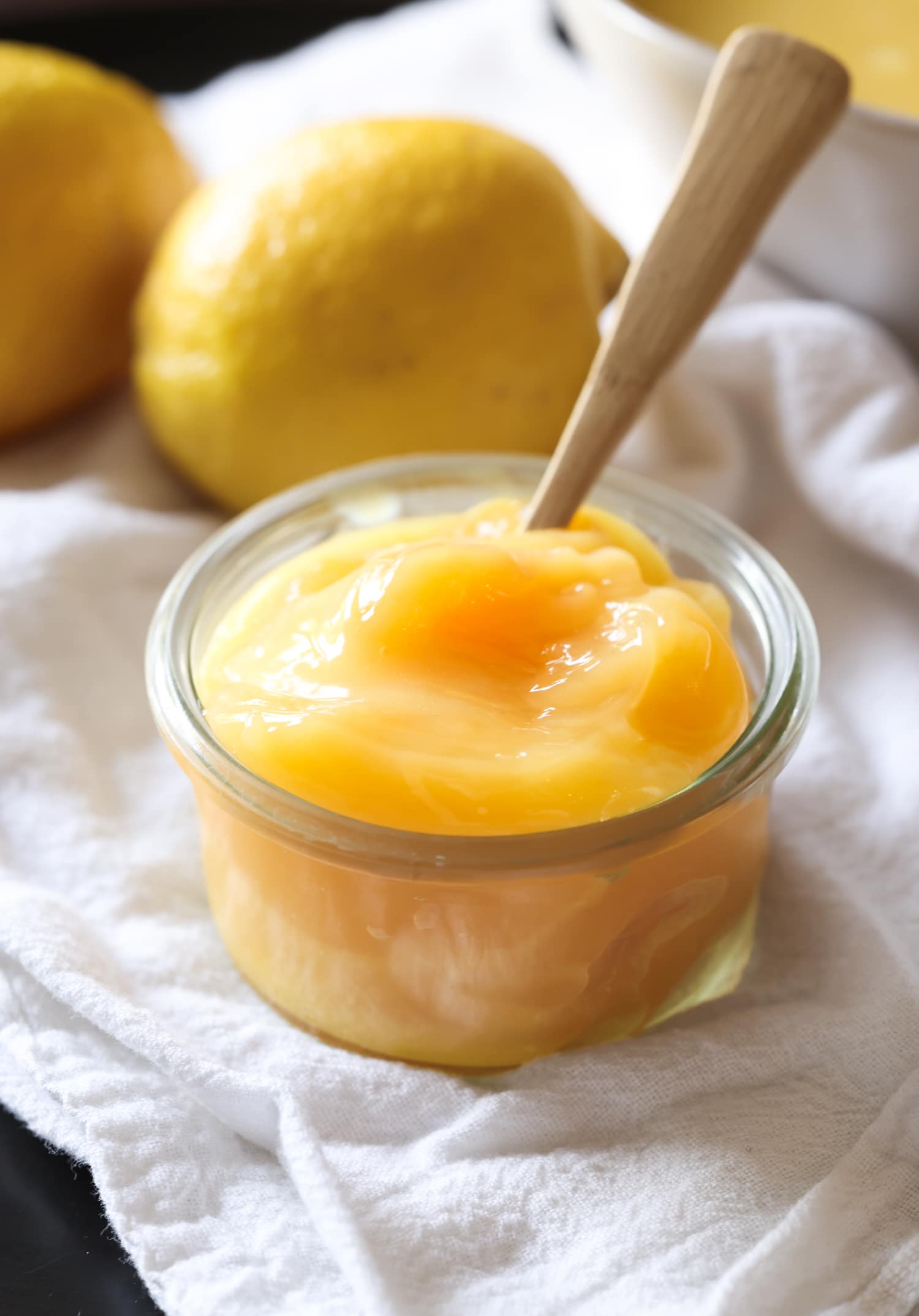 Mi receta casera de Lemon Curd es una crema de limón dulce perfecta para hornear, rellenar pasteles o tartas o como complemento para la crema del desayuno. Lemon Curd en un tarro de cristal con una cuchara
