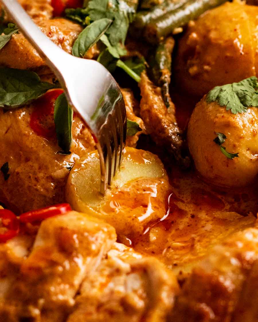 Tenedor recogiendo patatas en pollo asado al curry rojo tailandés