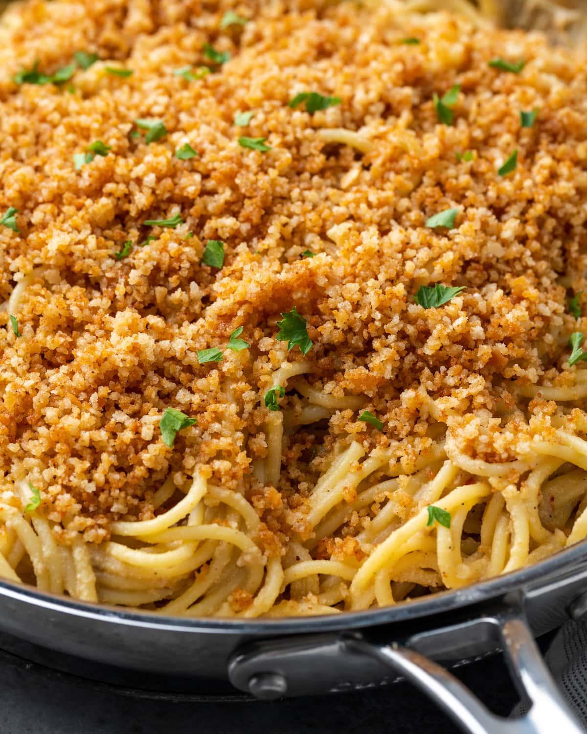 Primer plano de pasta César en una sartén cubierta con pan rallado con ajo y perejil.
