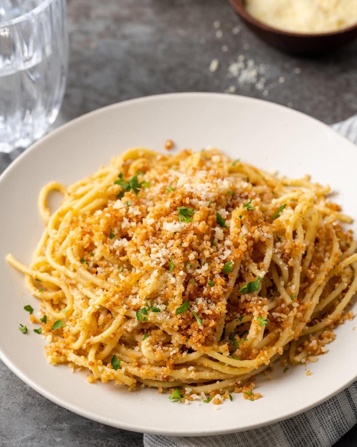 Una porción de pasta César en un plato blanco cubierto con pan rallado con ajo y perejil.