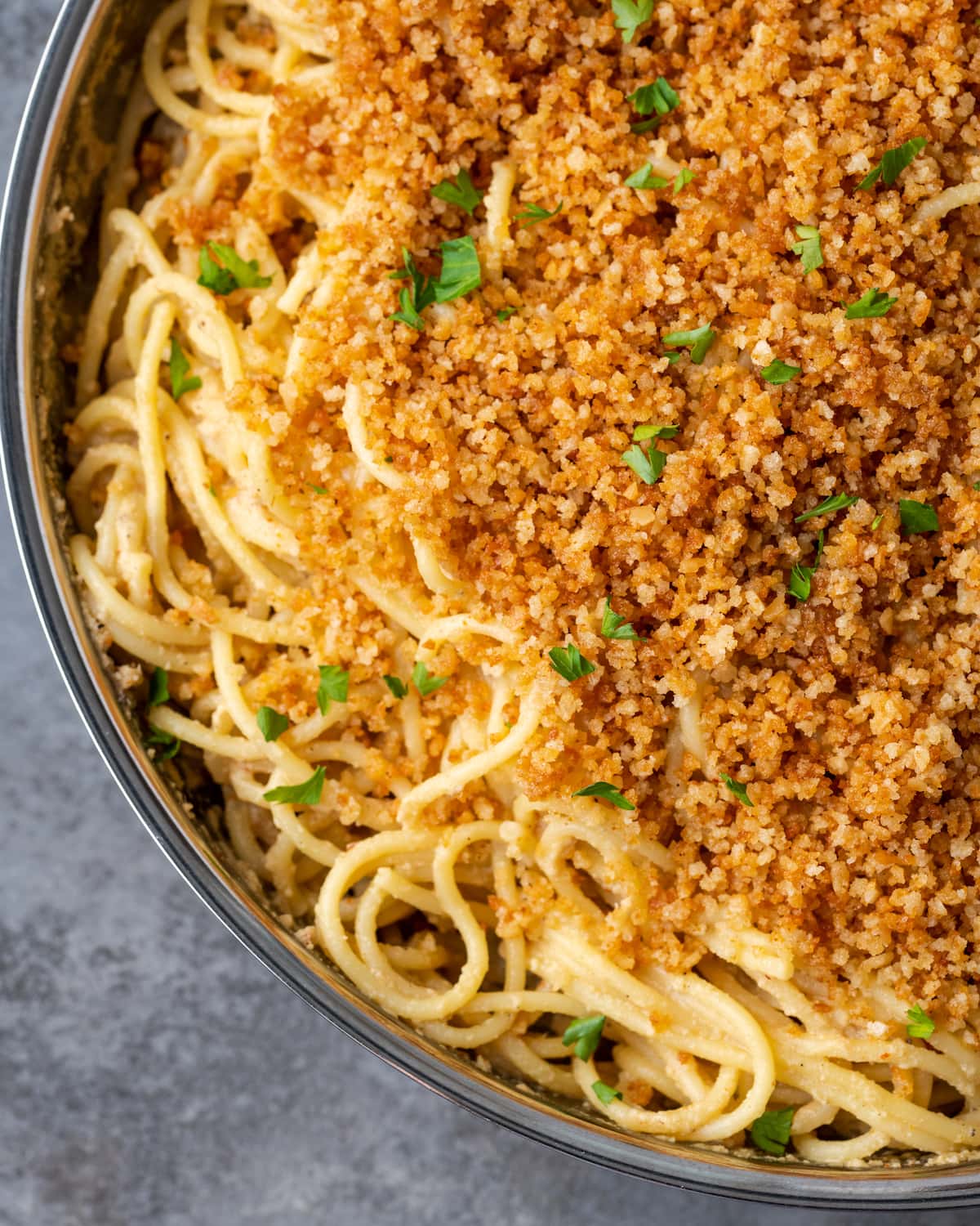 Primer plano de pasta César en una sartén cubierta con pan rallado con ajo y perejil.