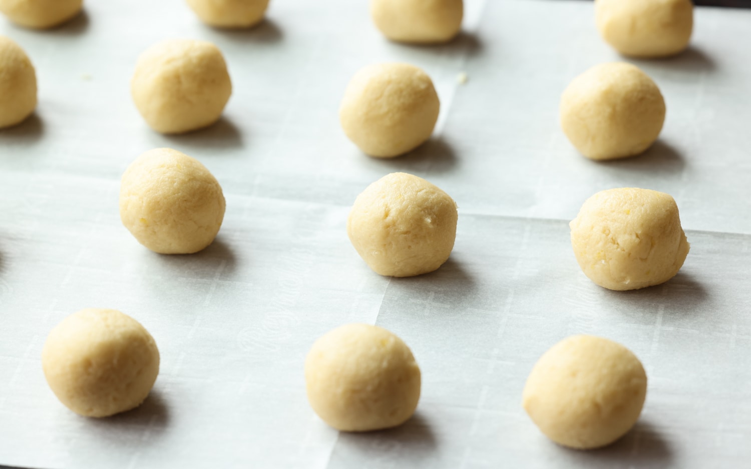 Mis galletas fáciles de enfriar con limón son galletas suaves, agrias y cítricas cubiertas con azúcar en polvo derretida. ¡La receta perfecta de galletas de limón! bolas de masa para galletas en una bandeja para hornear forrada de pergamino