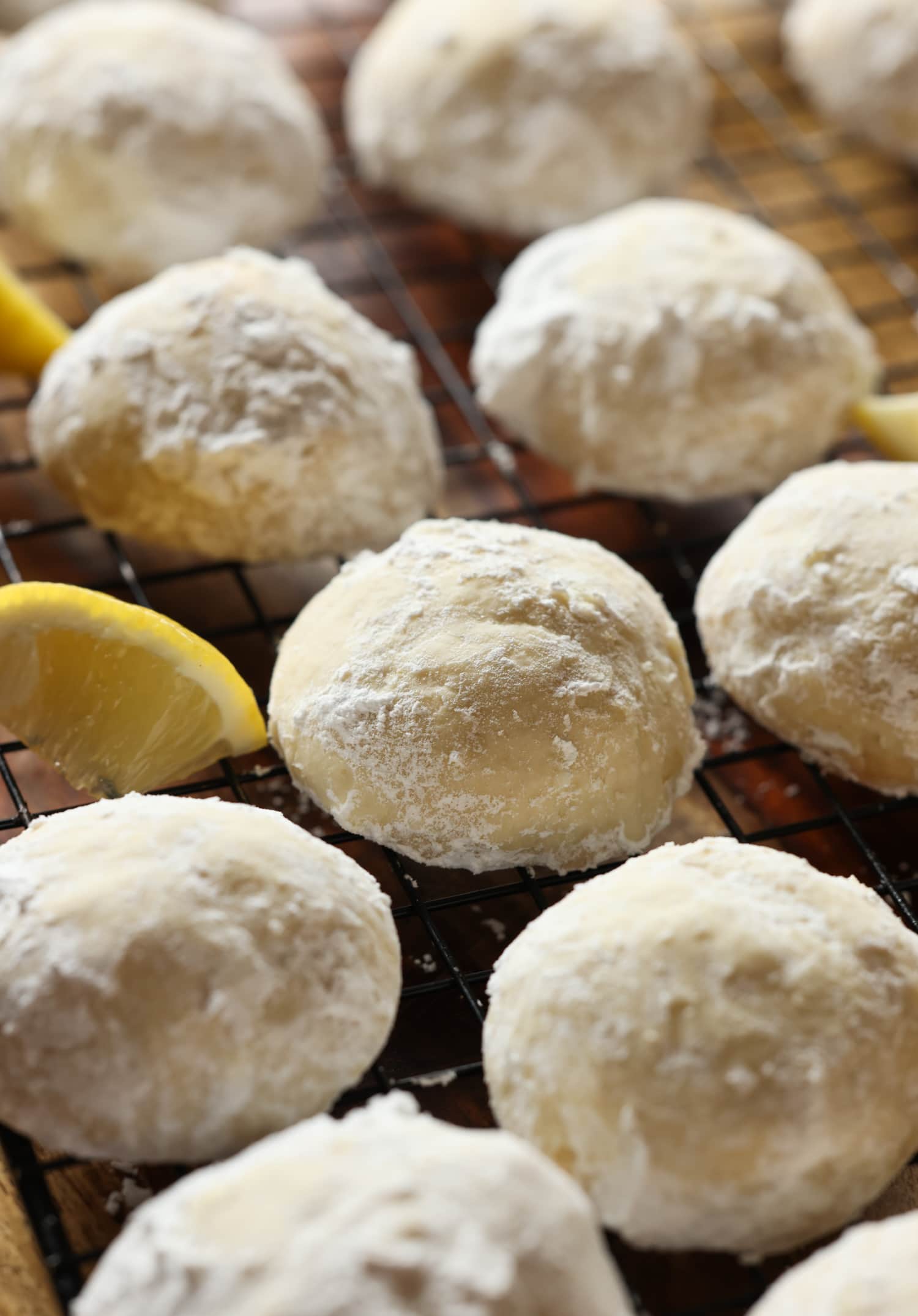 Mis galletas fáciles de enfriar con limón son galletas suaves, agrias y cítricas cubiertas con azúcar en polvo derretida. ¡La receta perfecta de galletas de limón! Sunshine Lemon Cooler Cookies en una rejilla para enfriar con rodajas de limón