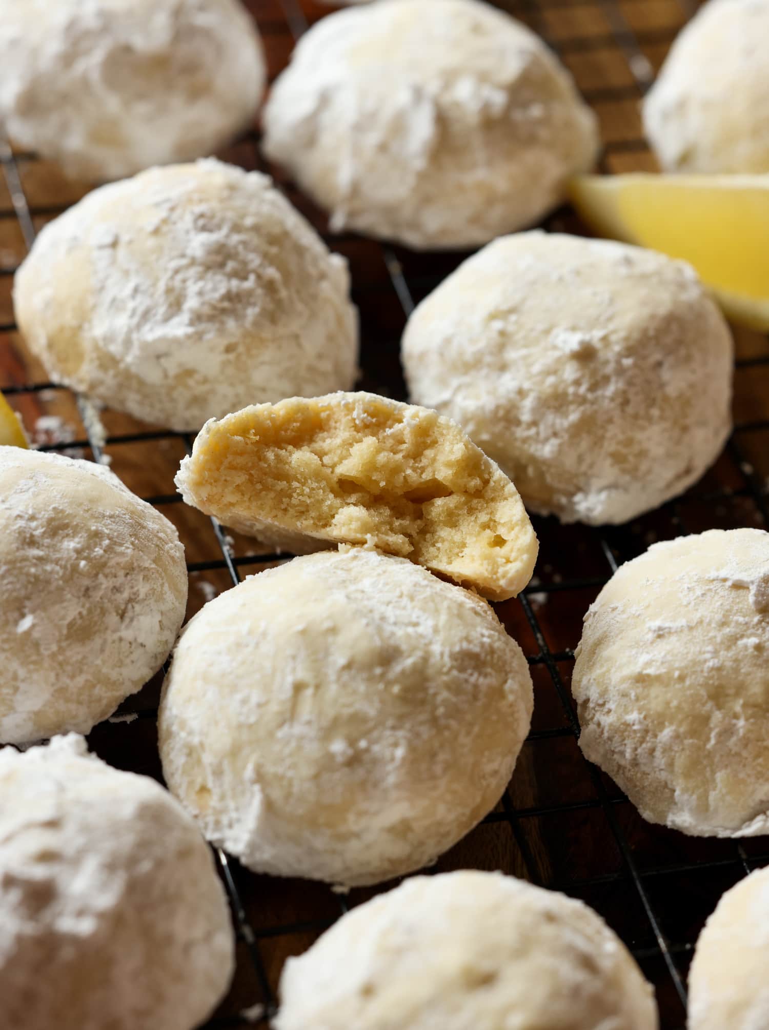 Mis galletas fáciles de enfriar con limón son galletas suaves, agrias y cítricas cubiertas con azúcar en polvo derretida. ¡La receta perfecta de galletas de limón! Galleta de limón recubierta de azúcar en polvo partida por la mitad en una rejilla para enfriar