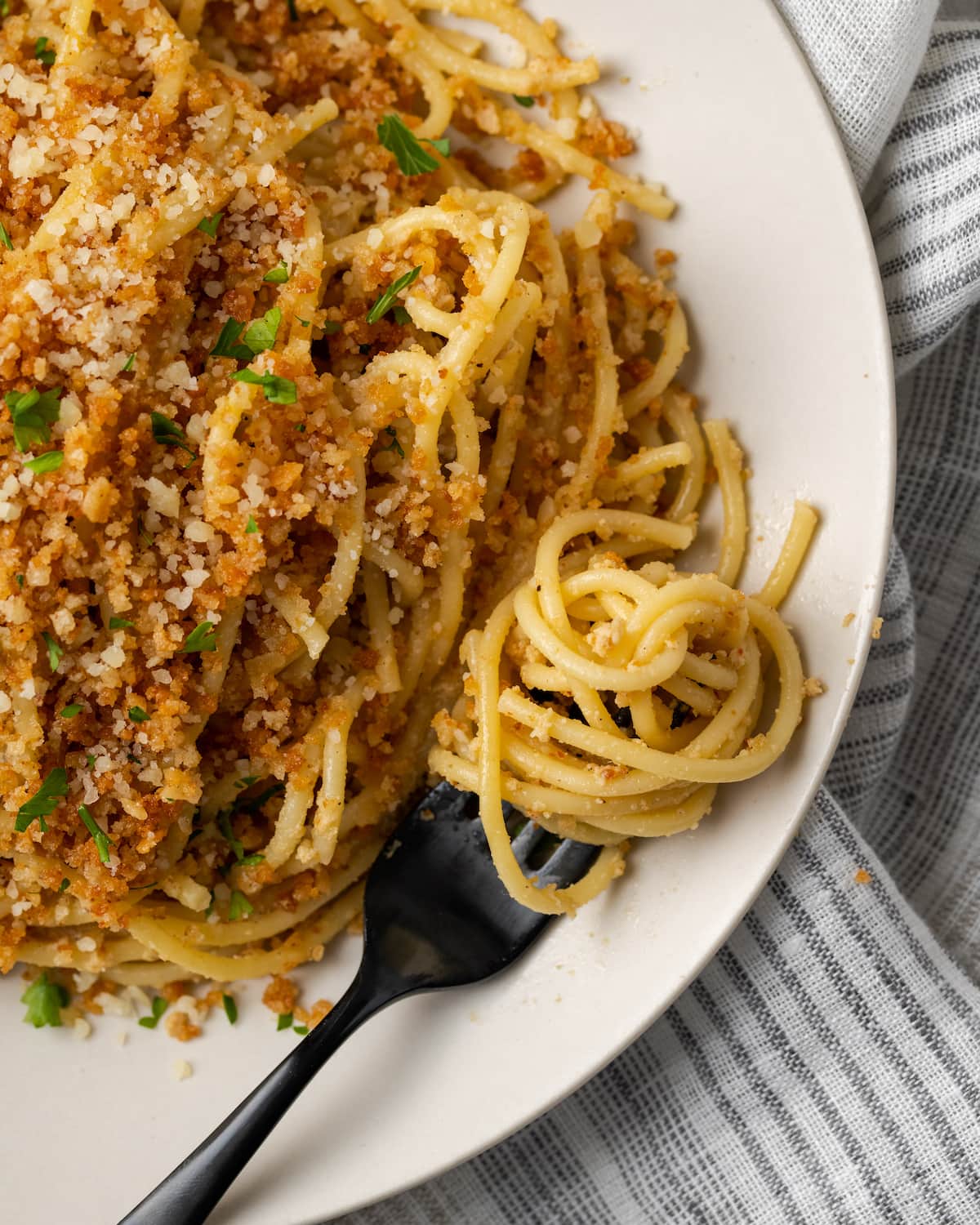 Vista aérea de la pasta César en un plato blanco cubierto con pan rallado de ajo y perejil, junto a la pasta arremolinada en un tenedor.