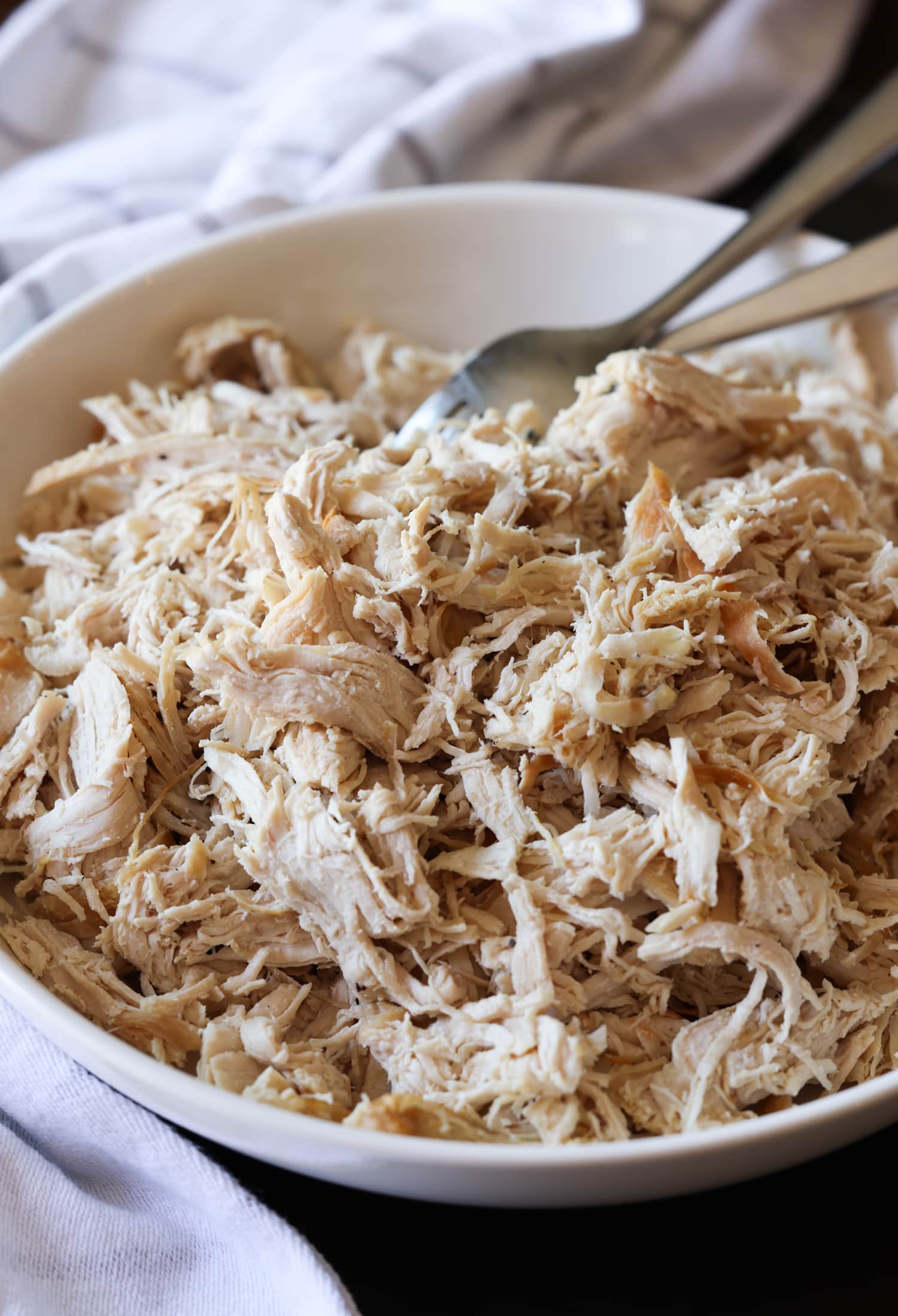 Aprende a hacer pollo desmenuzado de forma fácil y rápida con esta sencilla y deliciosa receta. ¡Perfecto para usar en ensaladas, guisos, tacos y más! Pechuga de pollo desmenuzada en un bol con tenedores