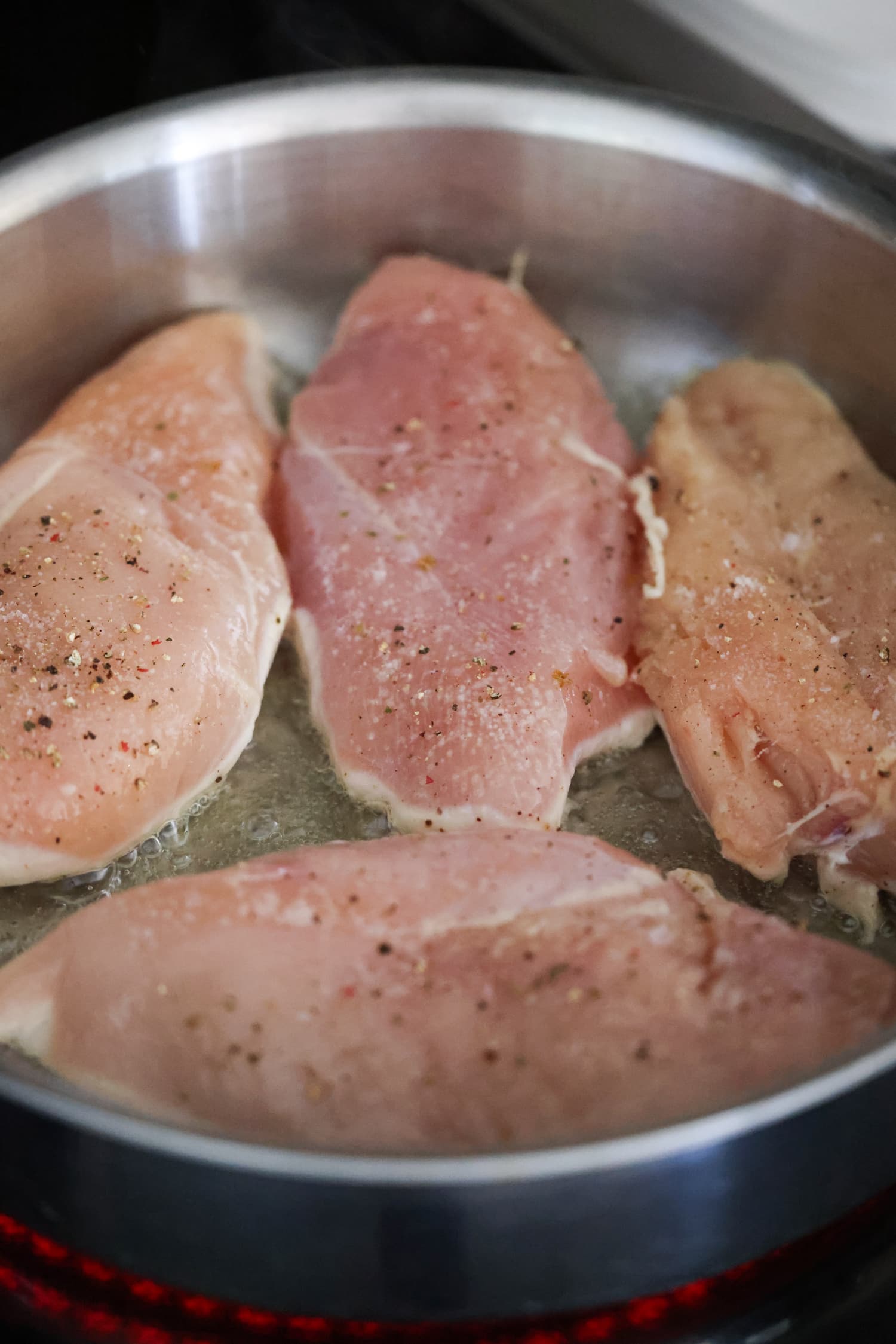 Aprende a hacer pollo desmenuzado de forma fácil y rápida con esta sencilla y deliciosa receta. ¡Perfecto para usar en ensaladas, guisos, tacos y más! pechugas de pollo crudas en una sartén cocinadas por un lado