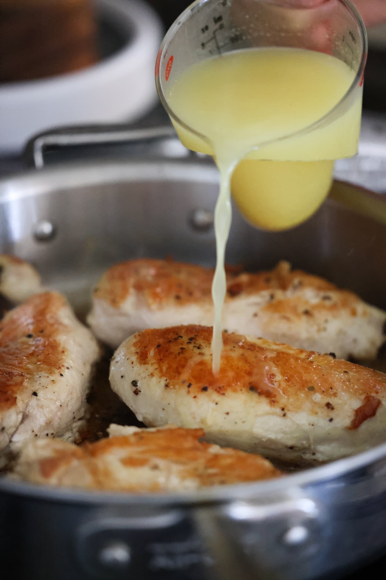 Aprende a hacer pollo desmenuzado de forma fácil y rápida con esta sencilla y deliciosa receta. ¡Perfecto para usar en ensaladas, guisos, tacos y más! agregando caldo de pollo en una sartén con pechugas de pollo