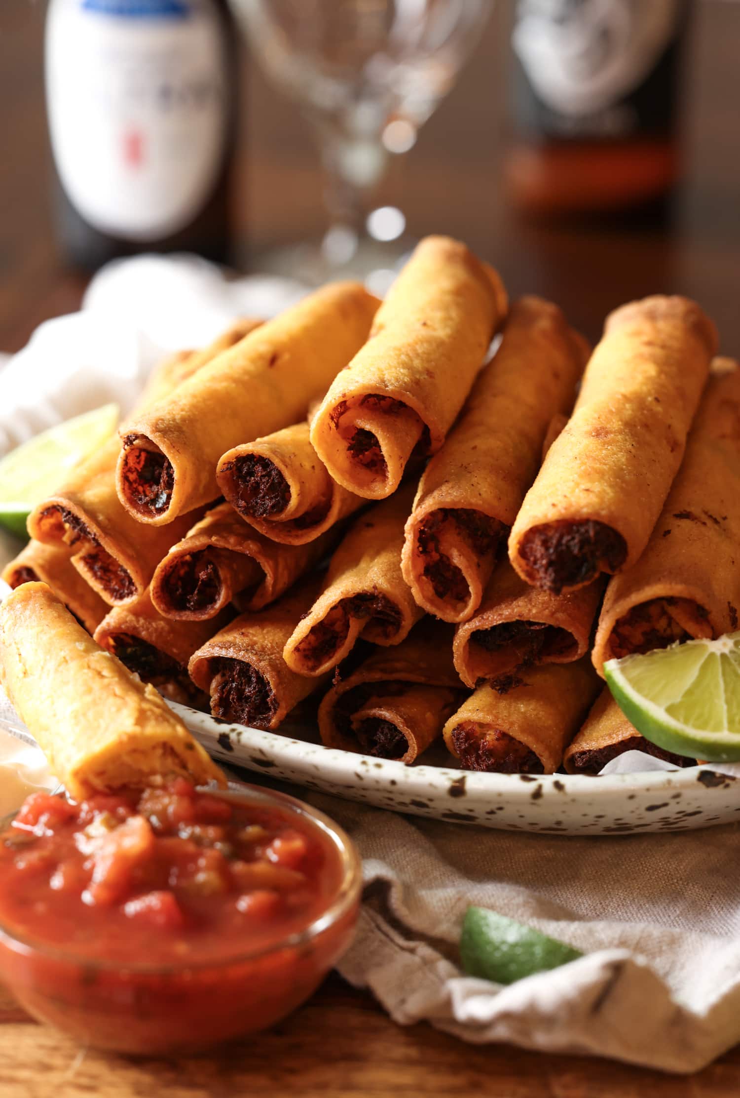 La receta de taquitos de pollo con queso son tortillas crujientes rellenas de pollo, quesos y condimentos, ¡una idea súper fácil para cenar en el área de los taquitos! taquitos en un plato con salsa y gajos de lima con cerveza