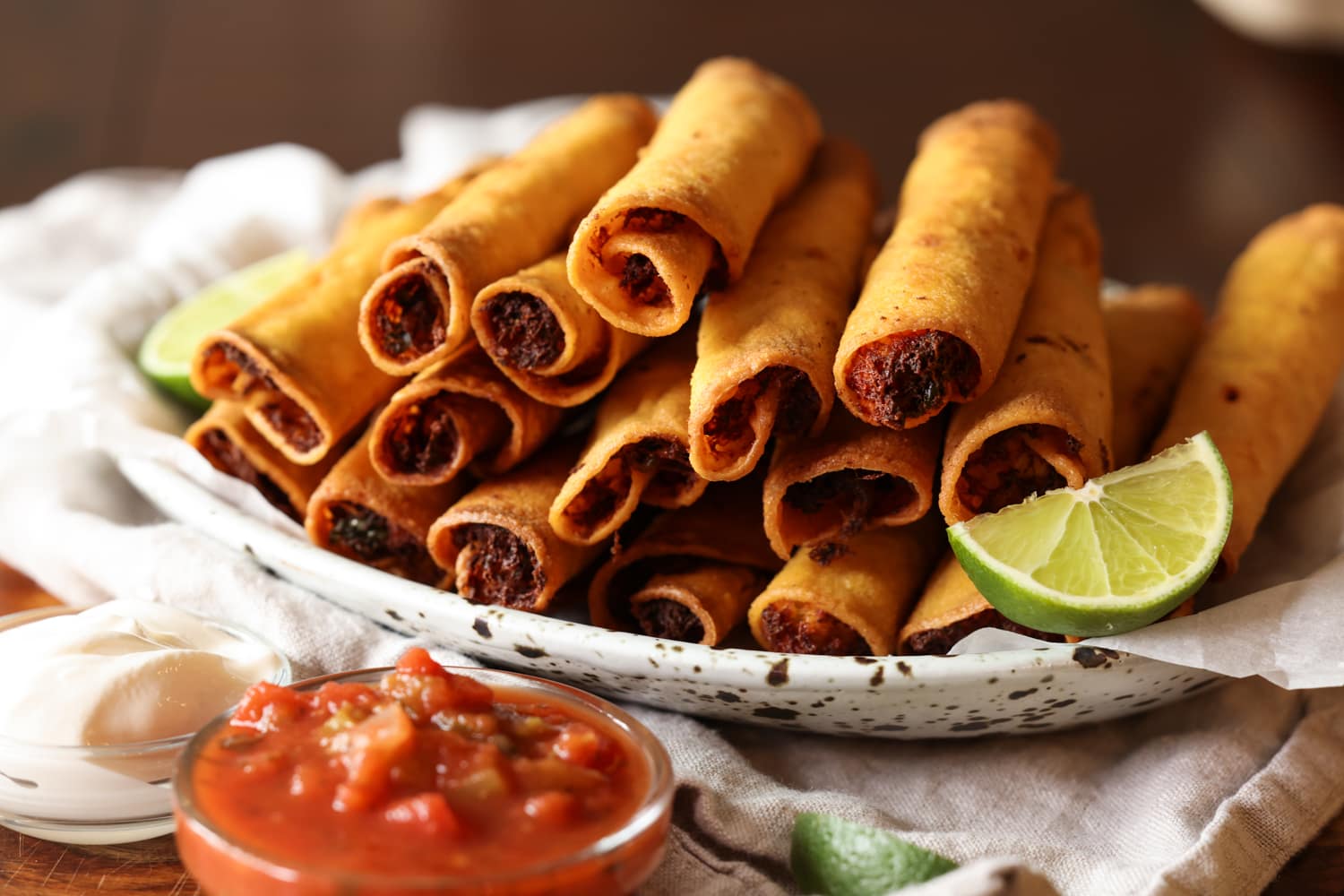 La receta de taquitos de pollo con queso son tortillas crujientes rellenas de pollo, quesos y condimentos, ¡una idea súper fácil para cenar en el área de los taquitos! taquitos de pollo dorados fritos en un plato con gajos de lima