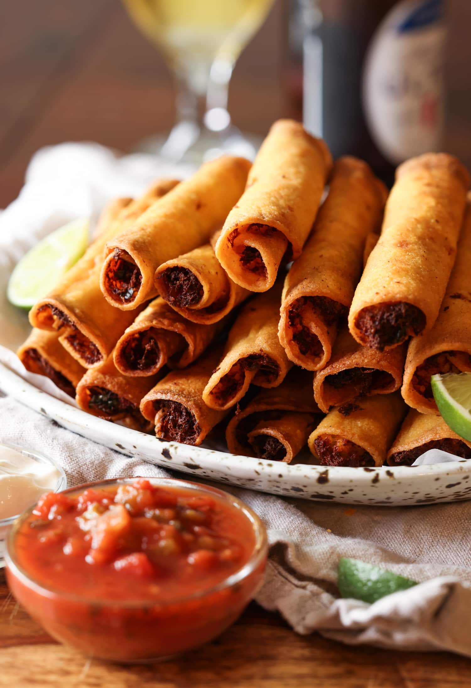 La receta de taquitos de pollo con queso son tortillas crujientes rellenas de pollo, quesos y condimentos, ¡una idea súper fácil para cenar en el área de los taquitos! taquitos de pollo apilados en un plato con salsa para mojar
