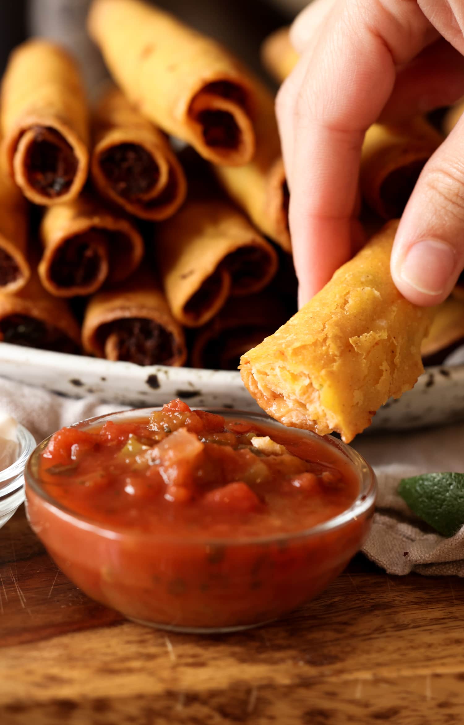 La receta de taquitos de pollo con queso son tortillas crujientes rellenas de pollo, quesos y condimentos, ¡una idea súper fácil para cenar en el área de los taquitos! un taquito sumergido en salsa