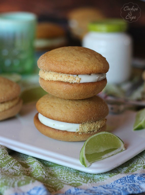 Dos pasteles whoopie de lima apilados en un plato blanco junto a una rodaja de lima.