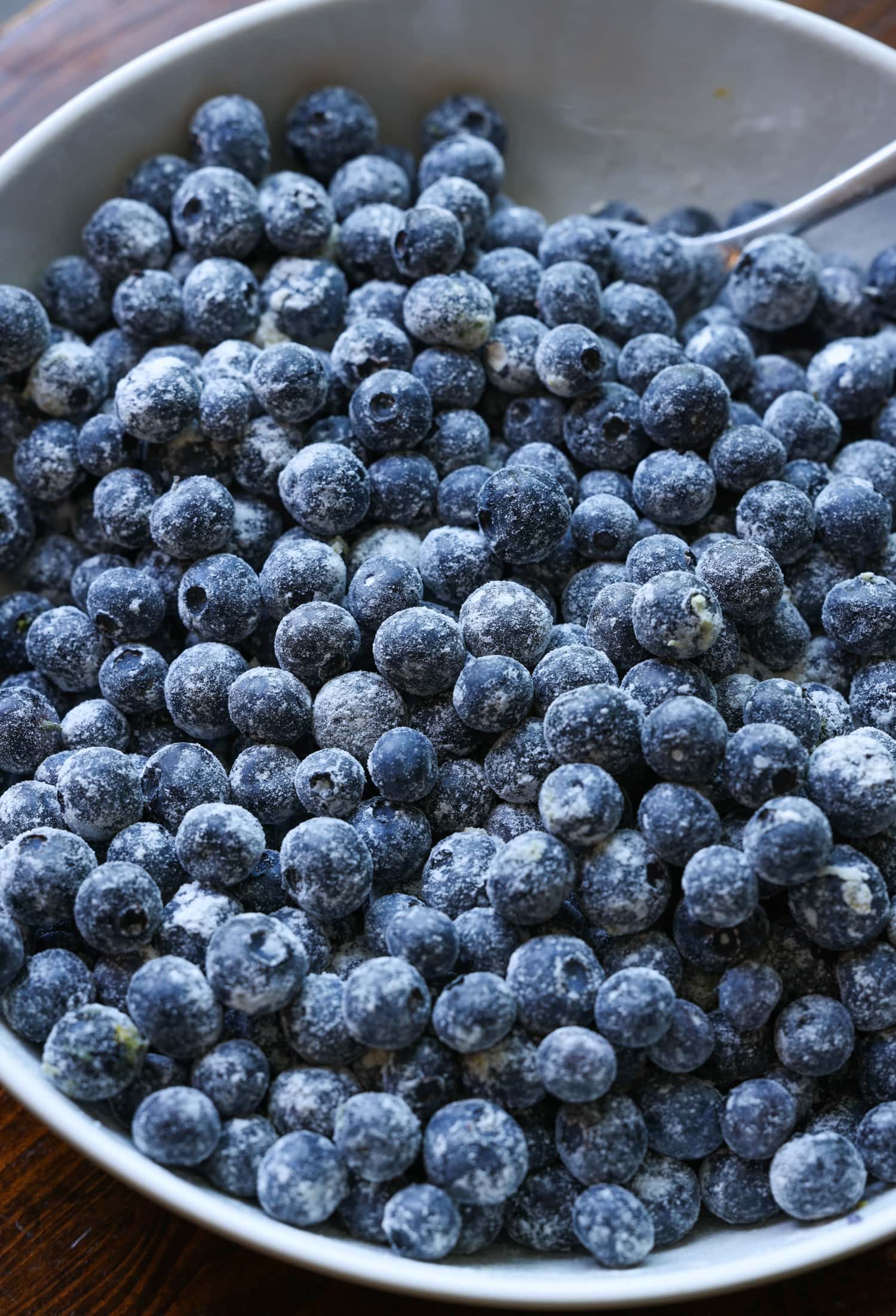 ¡Esta receta fácil de zapatero de arándanos es un postre clásico de verano que debes probar! Los arándanos dulces combinados con una cubierta de galleta mantecosa se hornean hasta que estén burbujeantes y dorados. arándanos recubiertos de azúcar y harina en un tazón blanco