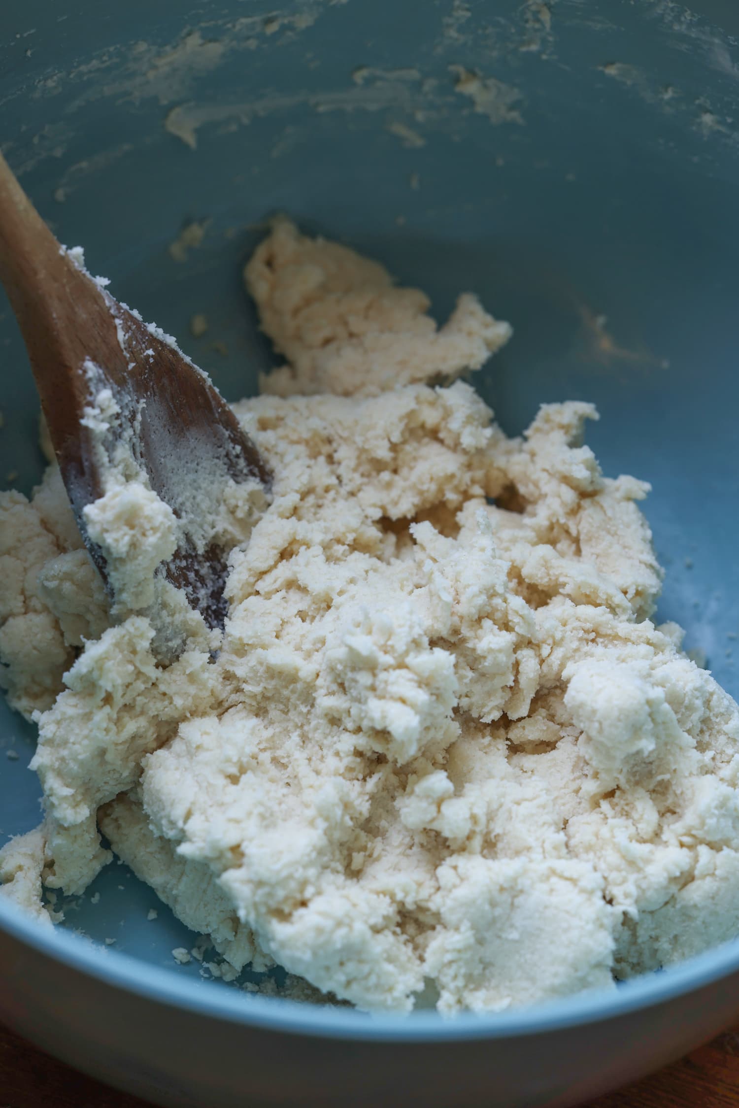 ¡Esta receta fácil de zapatero de arándanos es un postre clásico de verano que debes probar! Los arándanos dulces combinados con una cubierta de galleta mantecosa se hornean hasta que estén burbujeantes y dorados. masa de galletas en un tazón azul con una cuchara de madera