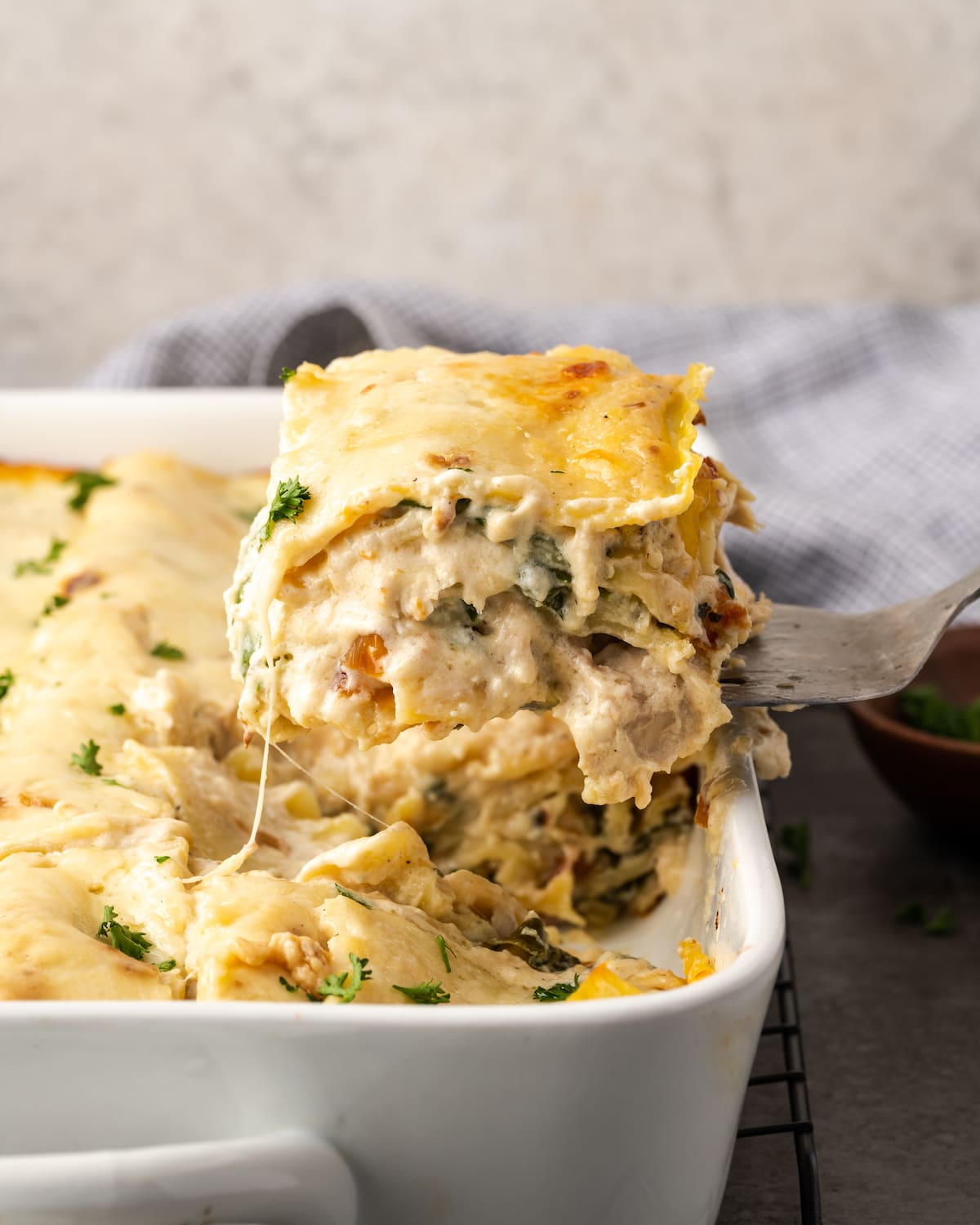 Lasaña cremosa de pollo rebosante de capas de pollo jugoso, fideos tiernos y salsa blanca casera sedosa con abundante queso derretido. Se levanta una rebanada de lasaña de pollo de una cacerola.