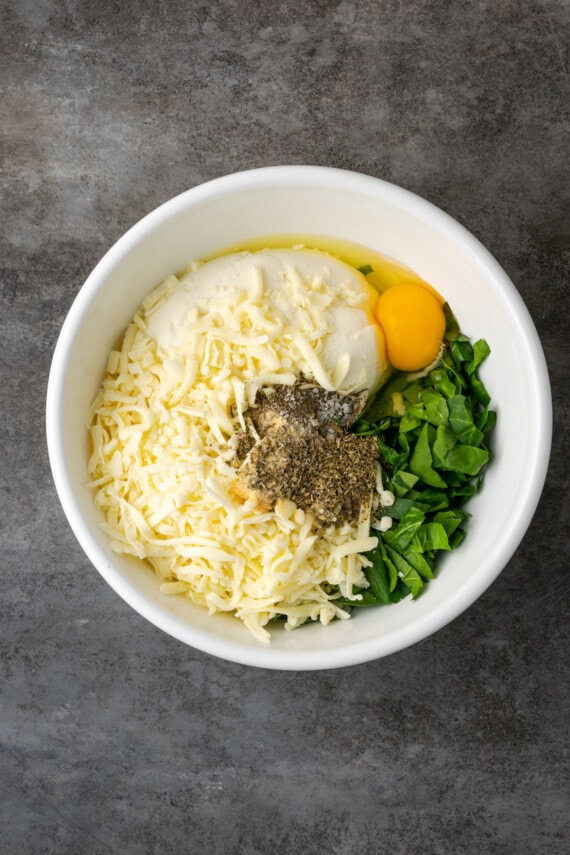 Lasaña cremosa de pollo rebosante de capas de pollo jugoso, fideos tiernos y salsa blanca casera sedosa con abundante queso derretido. Ingredientes de relleno de queso combinados en un tazón blanco.
