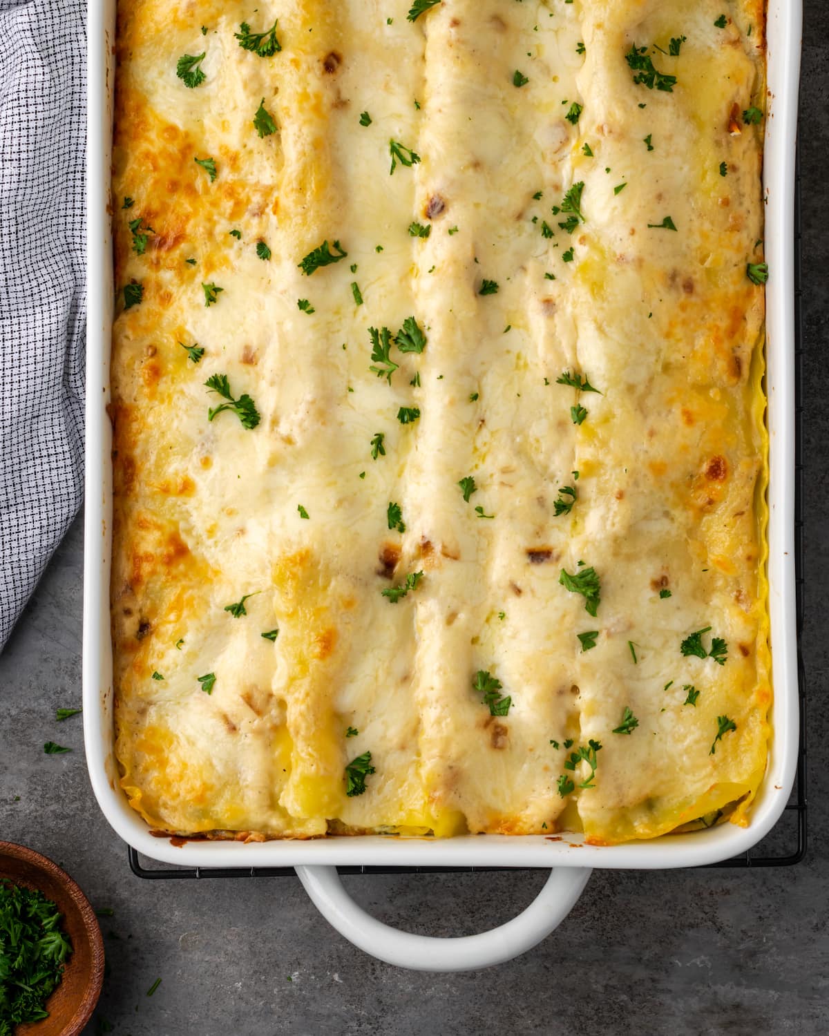 Lasaña cremosa de pollo rebosante de capas de pollo jugoso, fideos tiernos y salsa blanca casera sedosa con abundante queso derretido. Vista aérea de una lasaña de pollo al horno adornada con perejil picado.