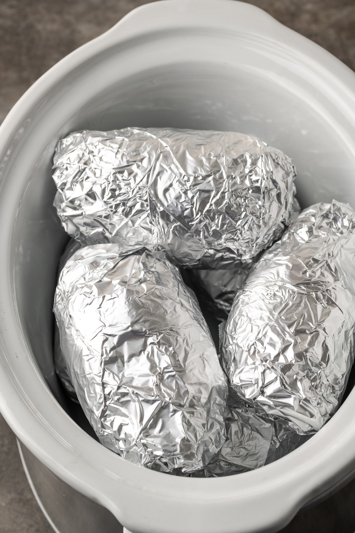 ¡Esta receta de papas al horno Crock Pot es un método más fácil para cocinar su guarnición de vegetales favorita sin encender el horno! Patatas envueltas en papel aluminio dentro de la olla de barro.