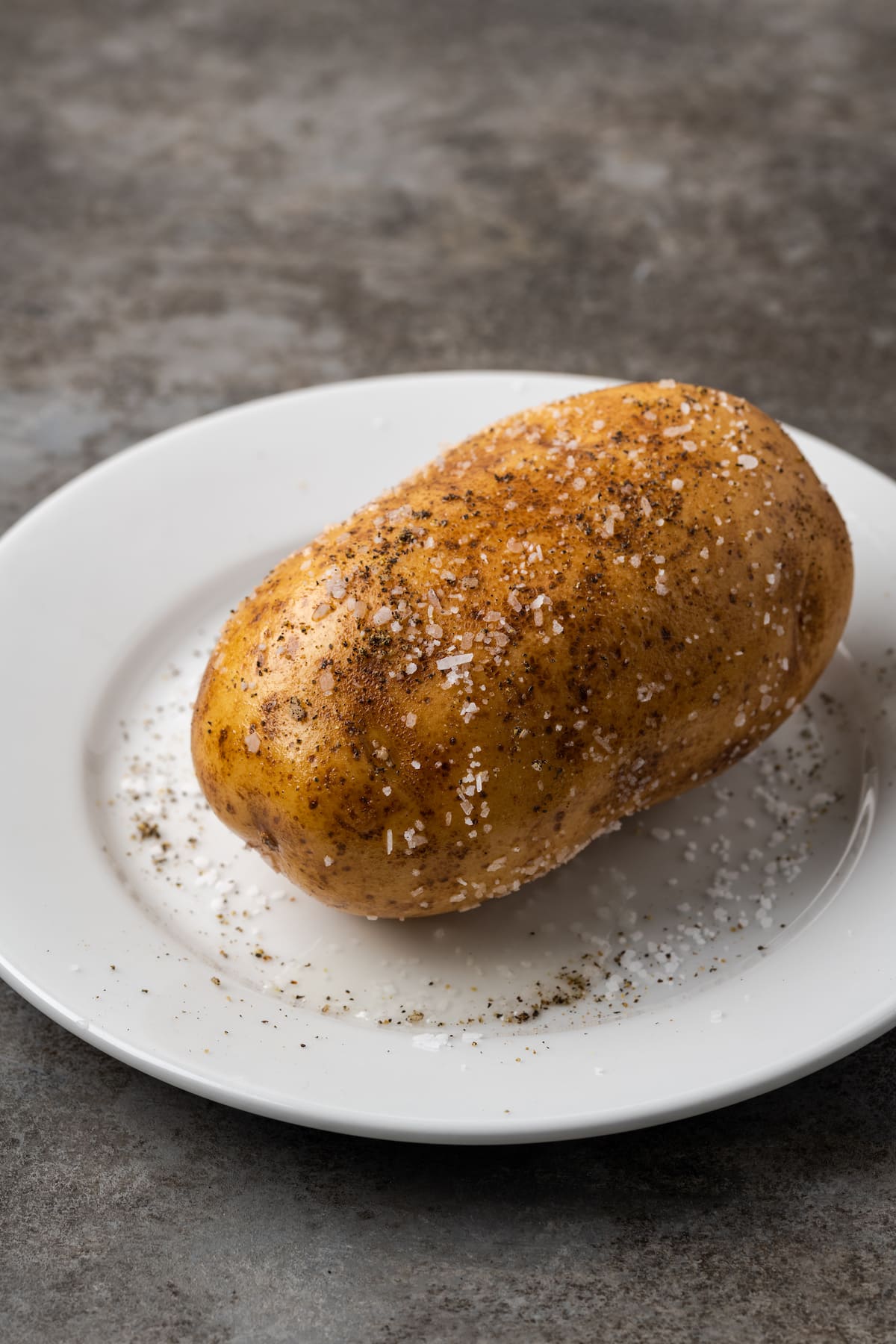 ¡Esta receta de papas al horno Crock Pot es un método más fácil para cocinar su guarnición de vegetales favorita sin encender el horno! Una papa sazonada con sal y pimienta en un plato blanco.