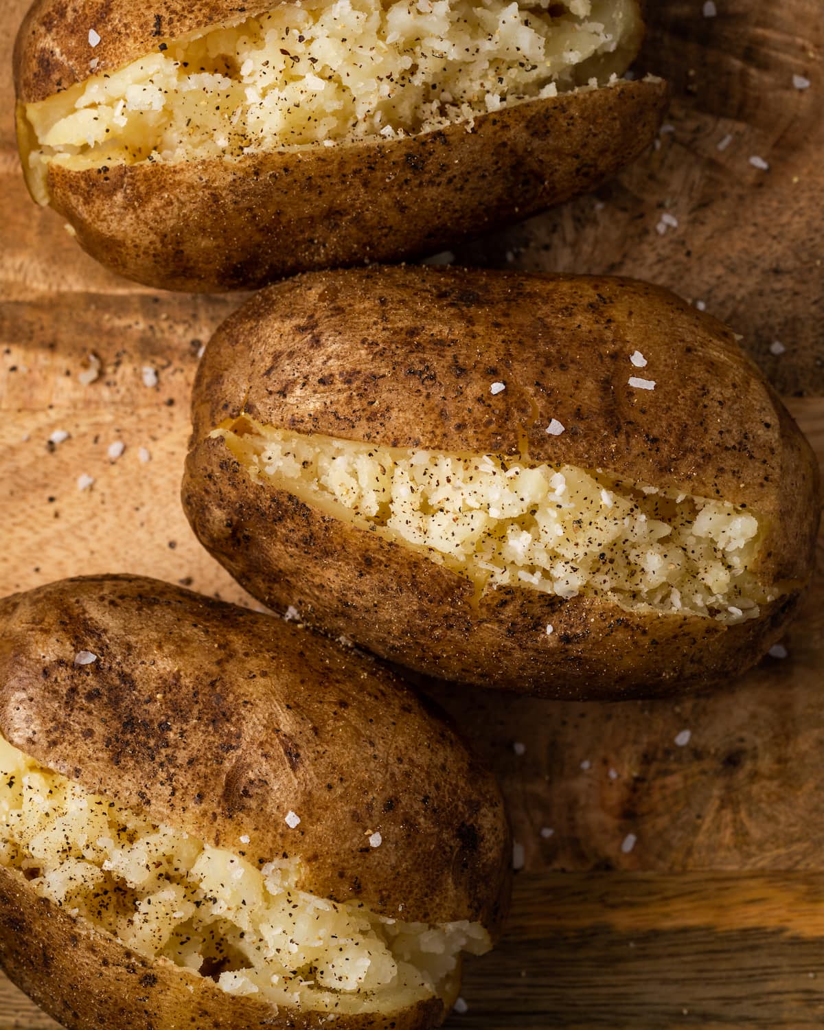 ¡Esta receta de papas al horno Crock Pot es un método más fácil para cocinar su guarnición de vegetales favorita sin encender el horno! Cerca de tres crock pot patatas al horno sobre una superficie de madera.