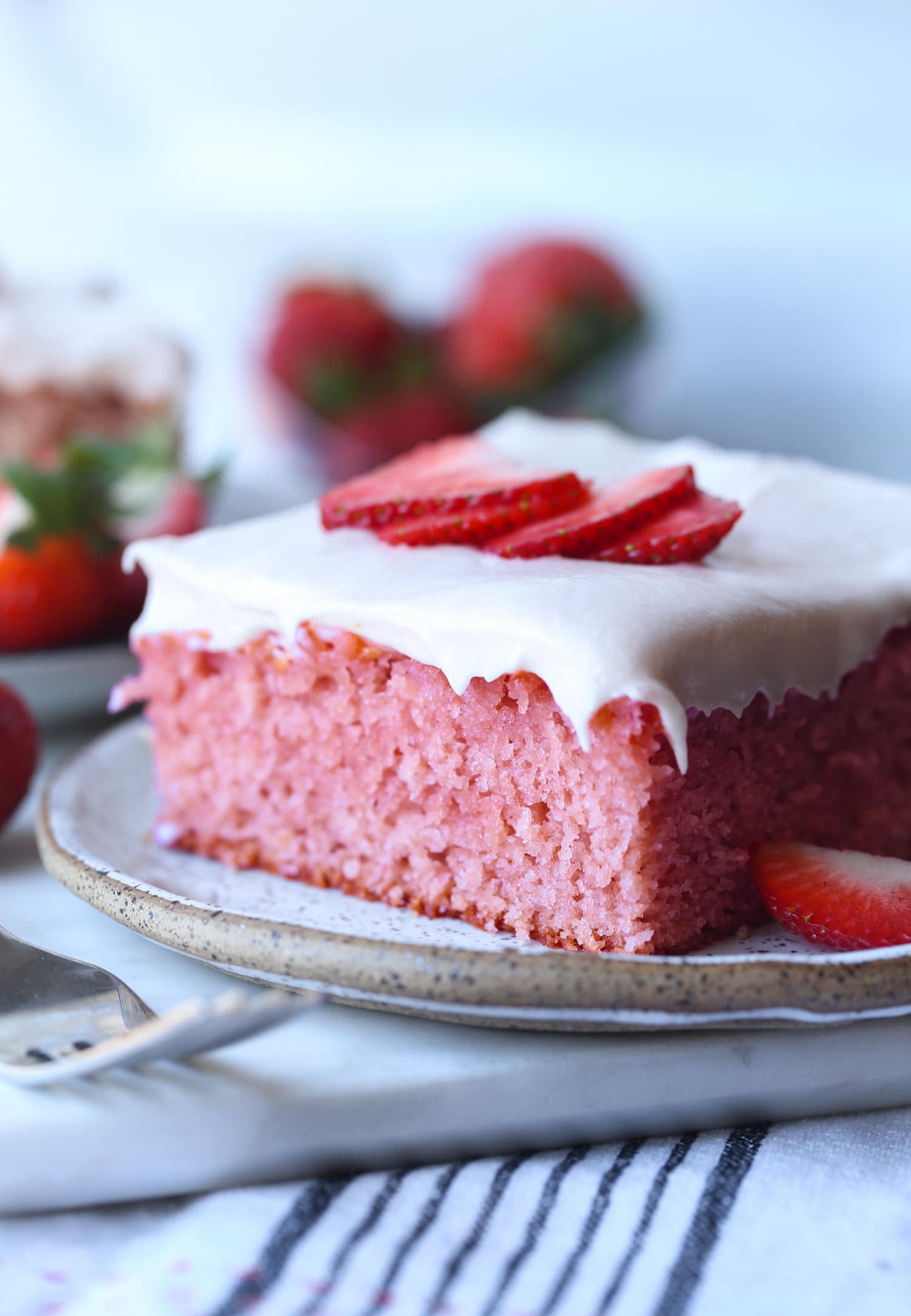 Rebanada de pastel de fresa en un plato cubierto con glaseado de queso crema y fresas frescas