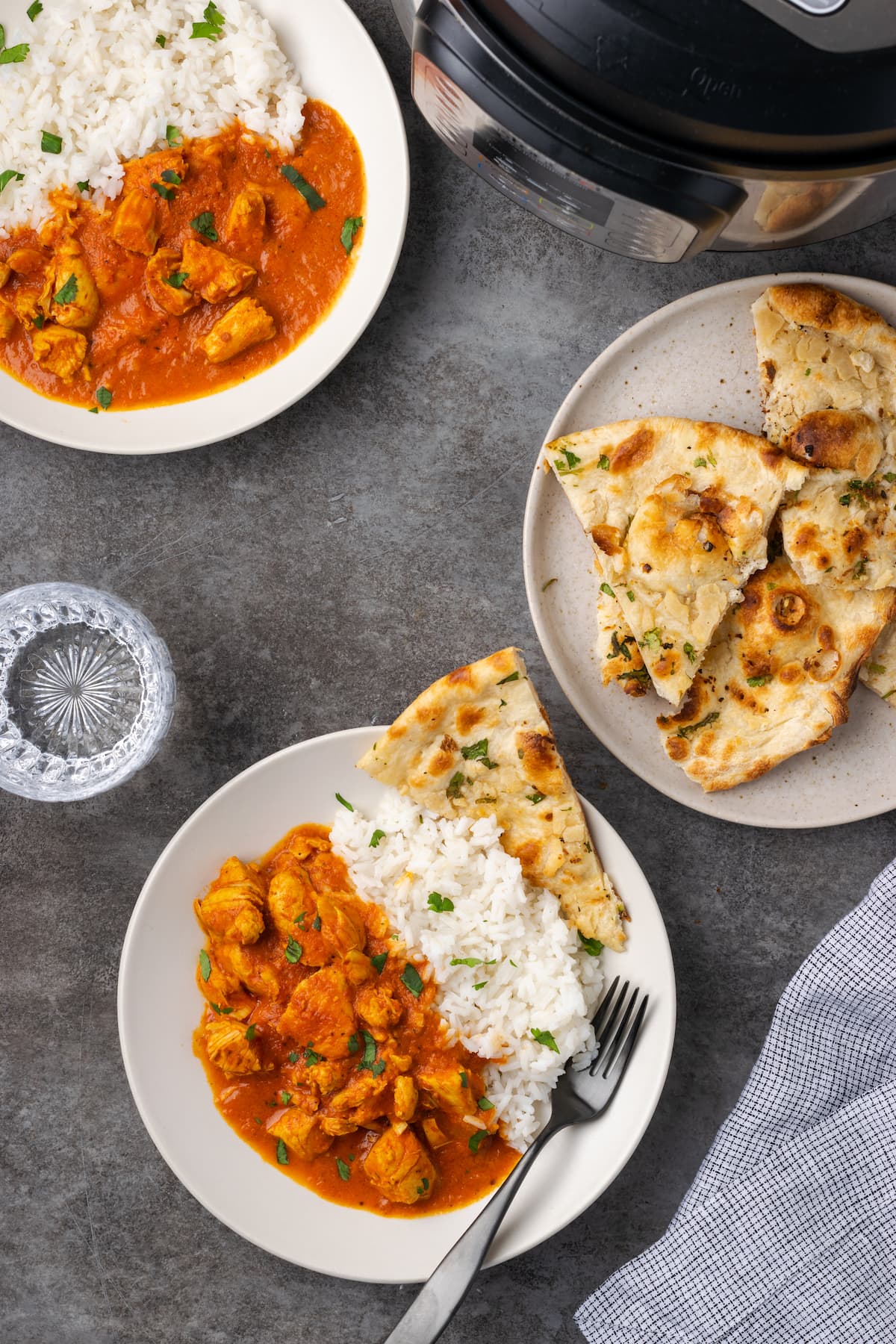 Vista aérea de dos platos llenos de pollo con mantequilla y una guarnición de arroz, junto a un plato de pan naan y el Instant Pot.