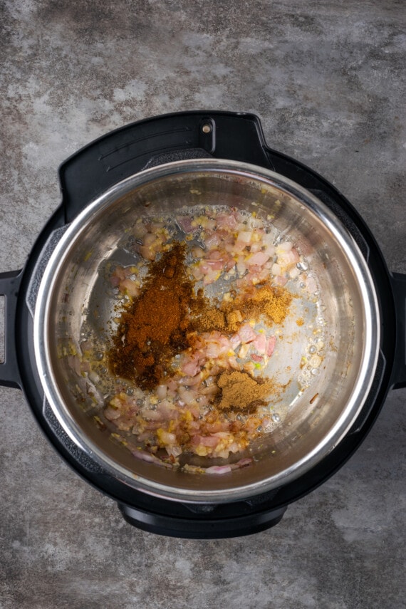 Especias agregadas a la olla instantánea con ajo y cebolla salteados.