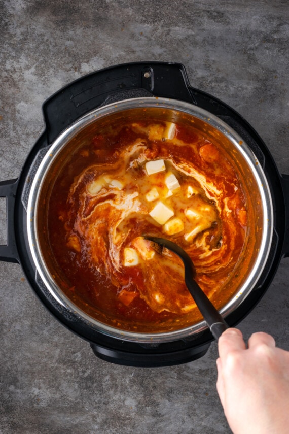 Una mano usa una cuchara para mezclar el pollo con mantequilla dentro de la olla instantánea.