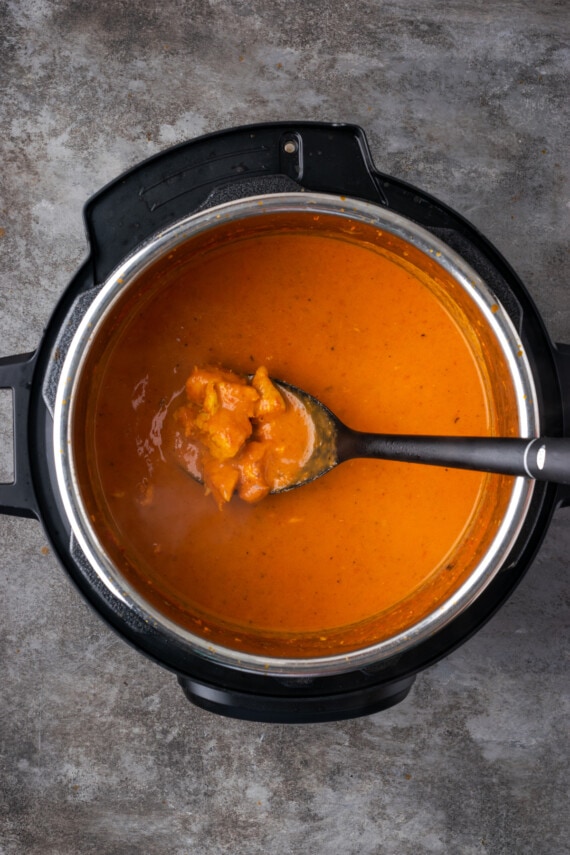 Una cucharada de pollo con mantequilla sostenida sobre la olla instantánea.
