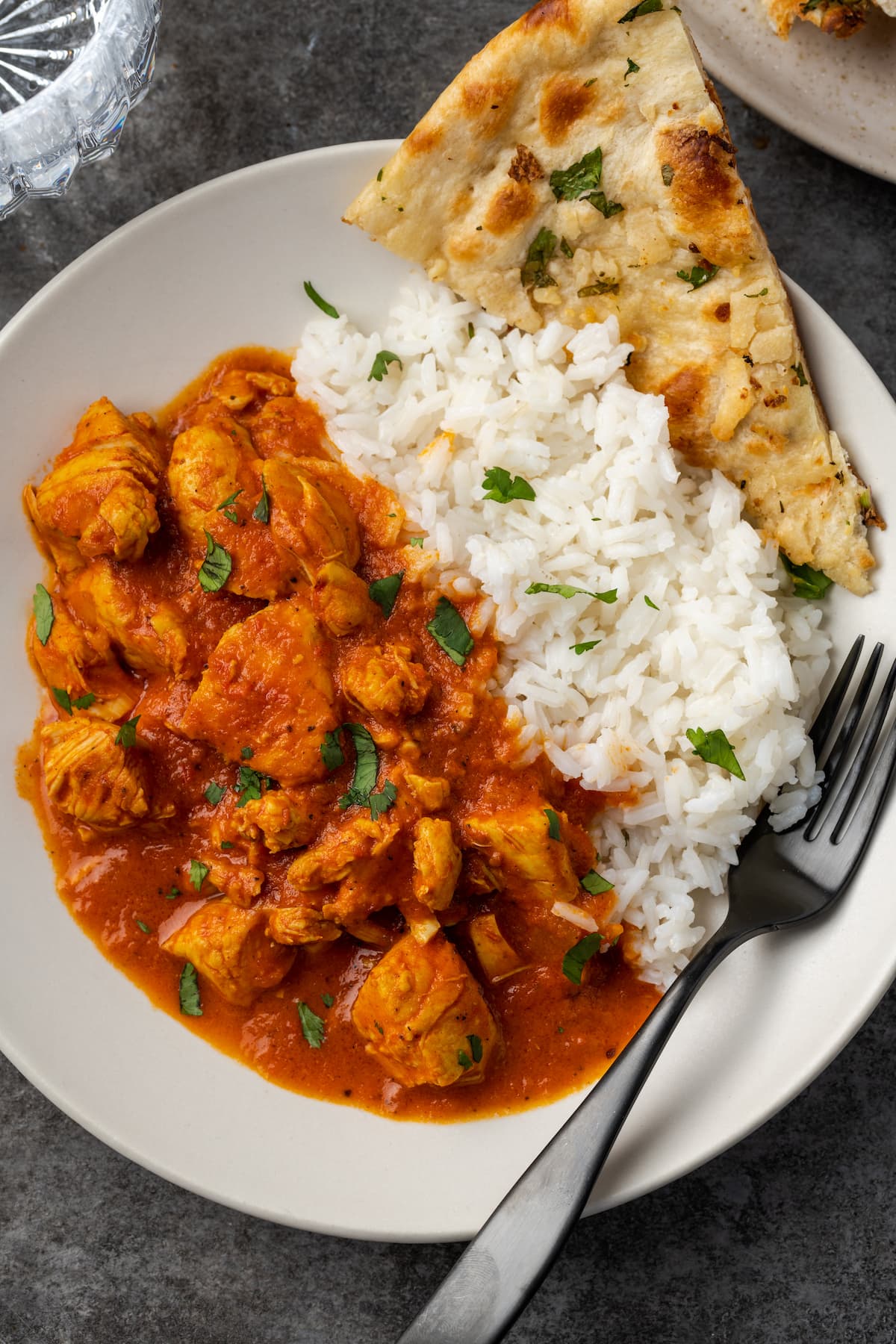 Vista aérea de pollo instantáneo con mantequilla de olla servido en un plato blanco junto a un lado de arroz basmati y naan, adornado con cilantro fresco picado.