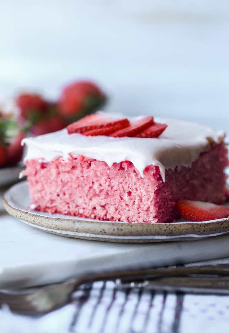 una rebanada de pastel de fresas en un plato cubierto con rodajas de fresas frescas