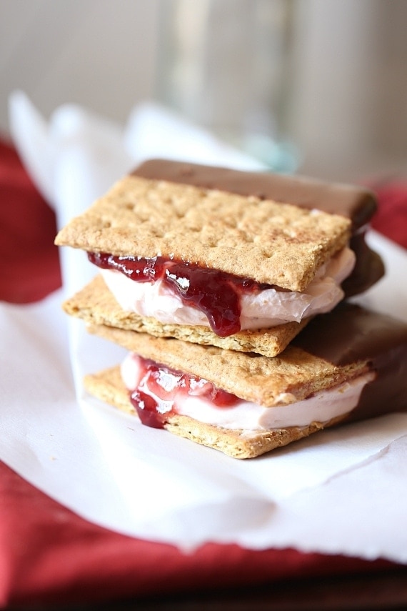 Dos sándwiches de tarta de queso y fresas bañados en chocolate apilados sobre un paño blanco.