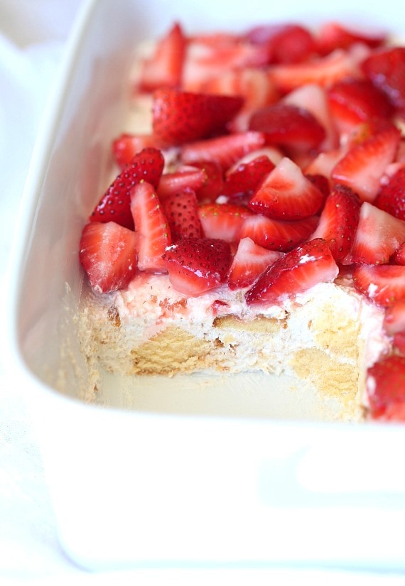 Tarta de fresas de la empresa en una fuente para horno blanca a la que le falta una porción.