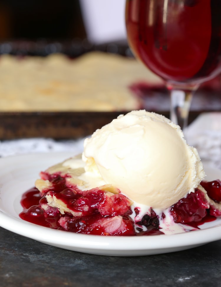 Una rebanada de Berry Slab Pie en un plato blanco cubierto con una bola de helado de vainilla.