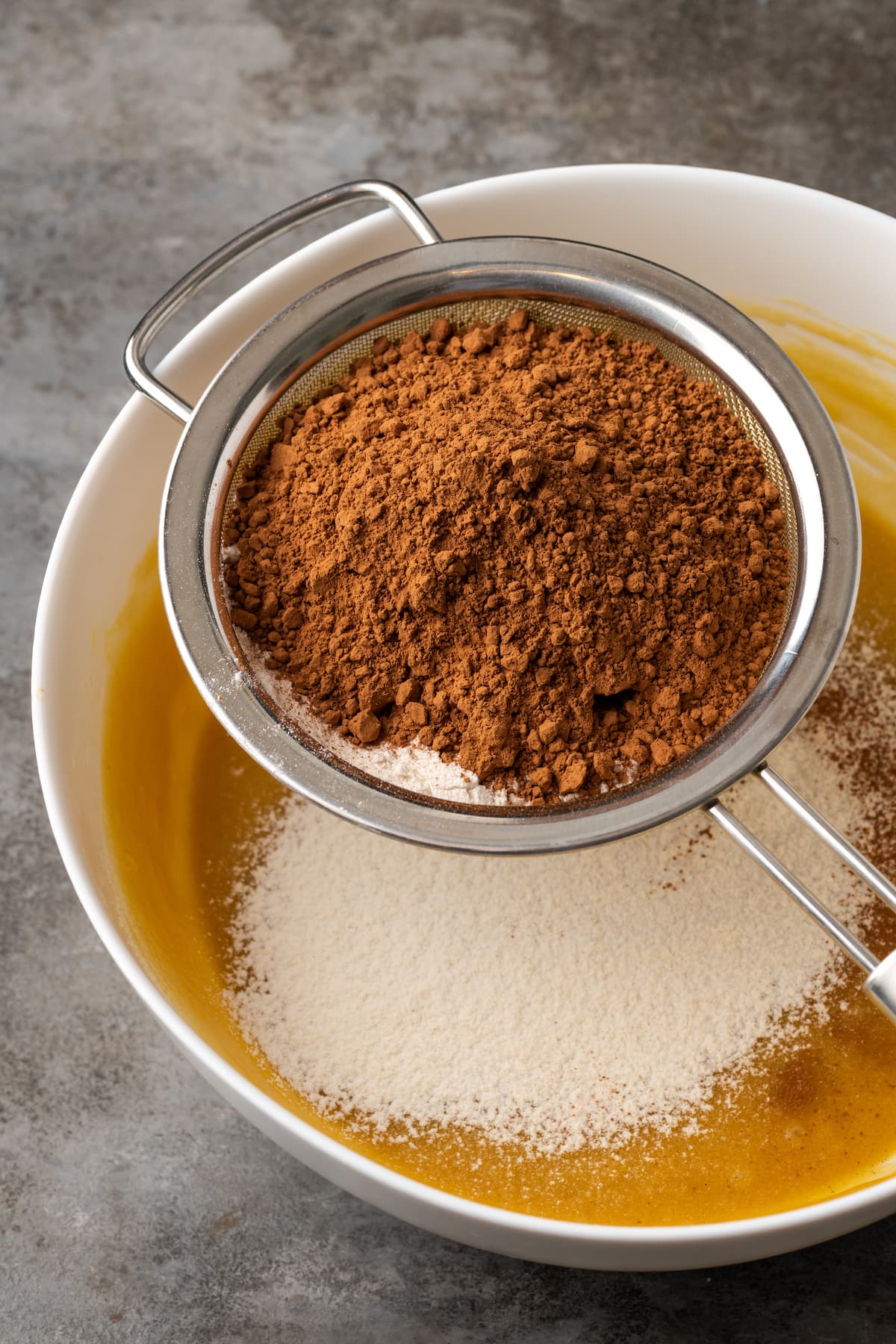 Ingredientes secos tamizados a través de un tamiz de malla fina sobre un tazón de ingredientes para la masa de brownie.