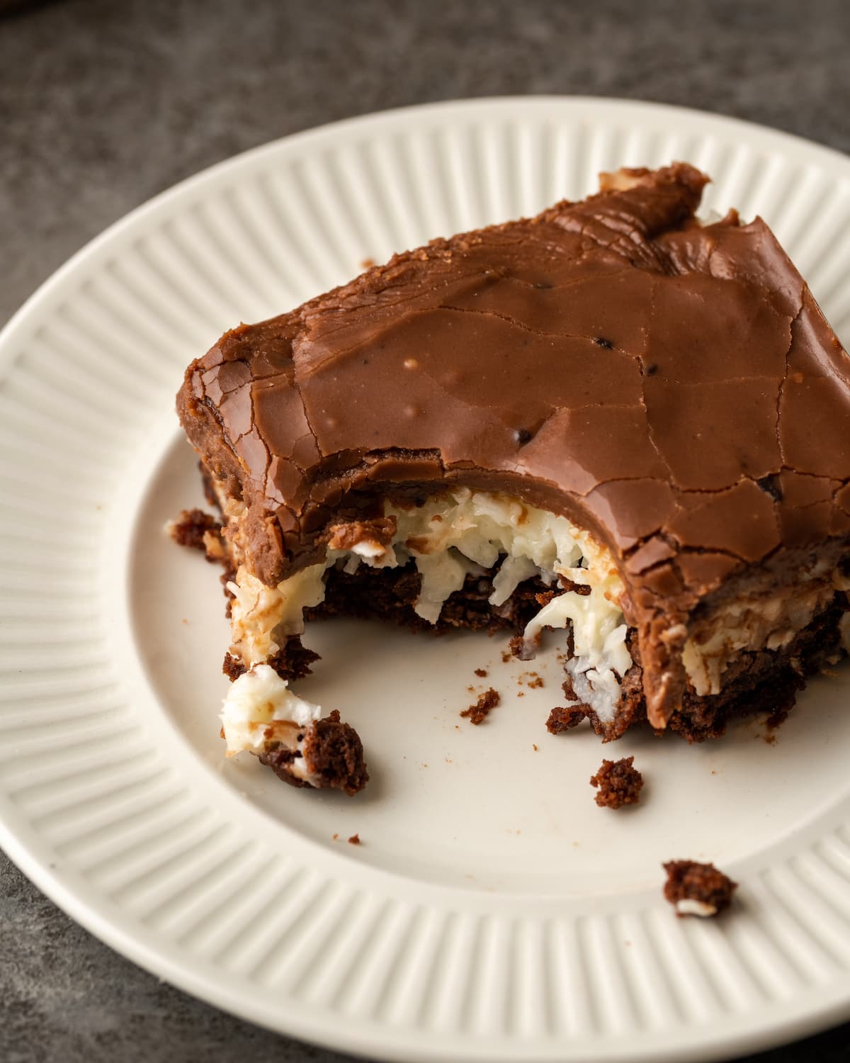 Un brownie de coco al que le falta un bocado en un plato blanco.
