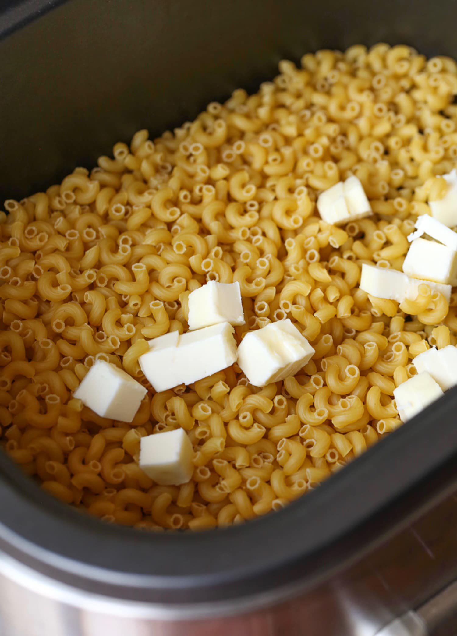 Cubos de mantequilla sobre pasta cruda en una olla de barro