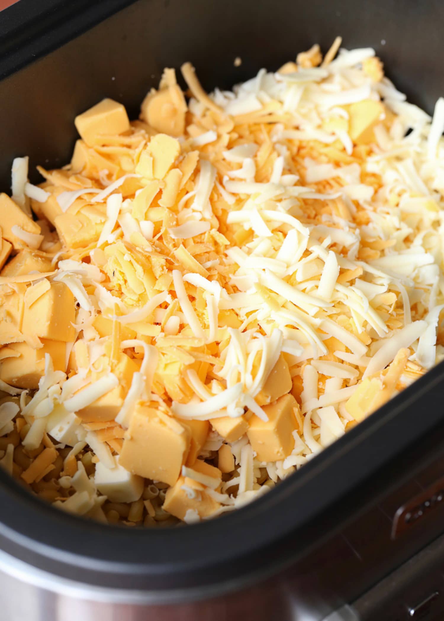 Queso rallado sobre pasta en una olla de cocción lenta preparando macarrones con queso