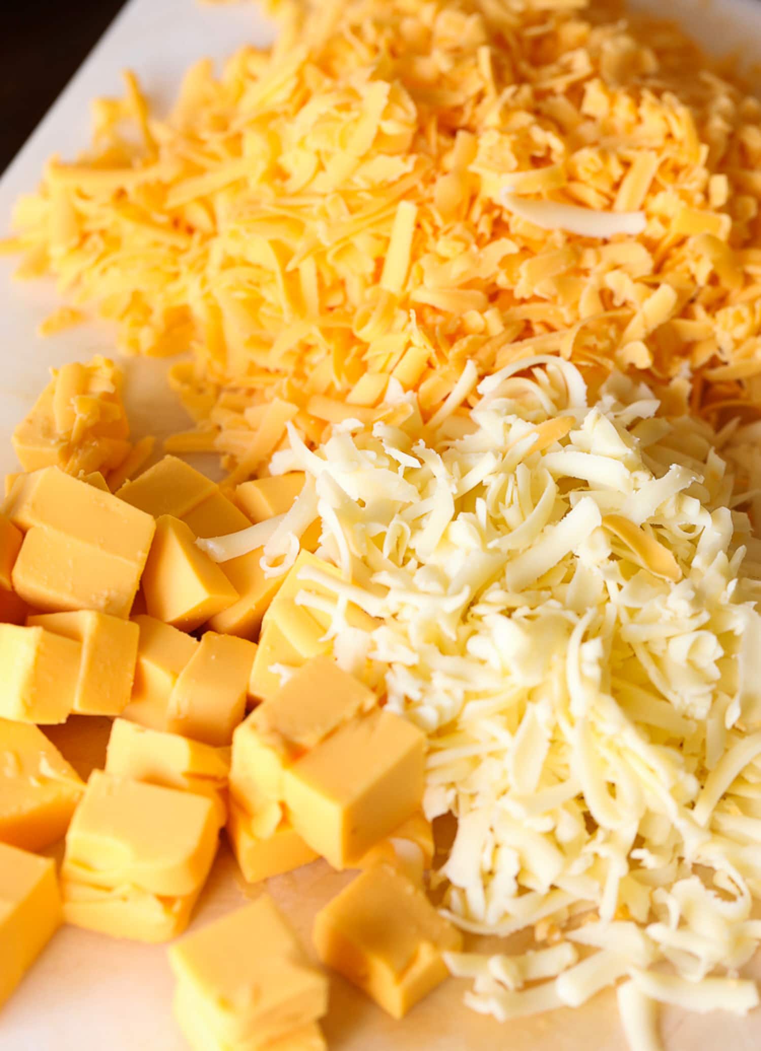 tres tipos de queso rallado en una tabla para cortar