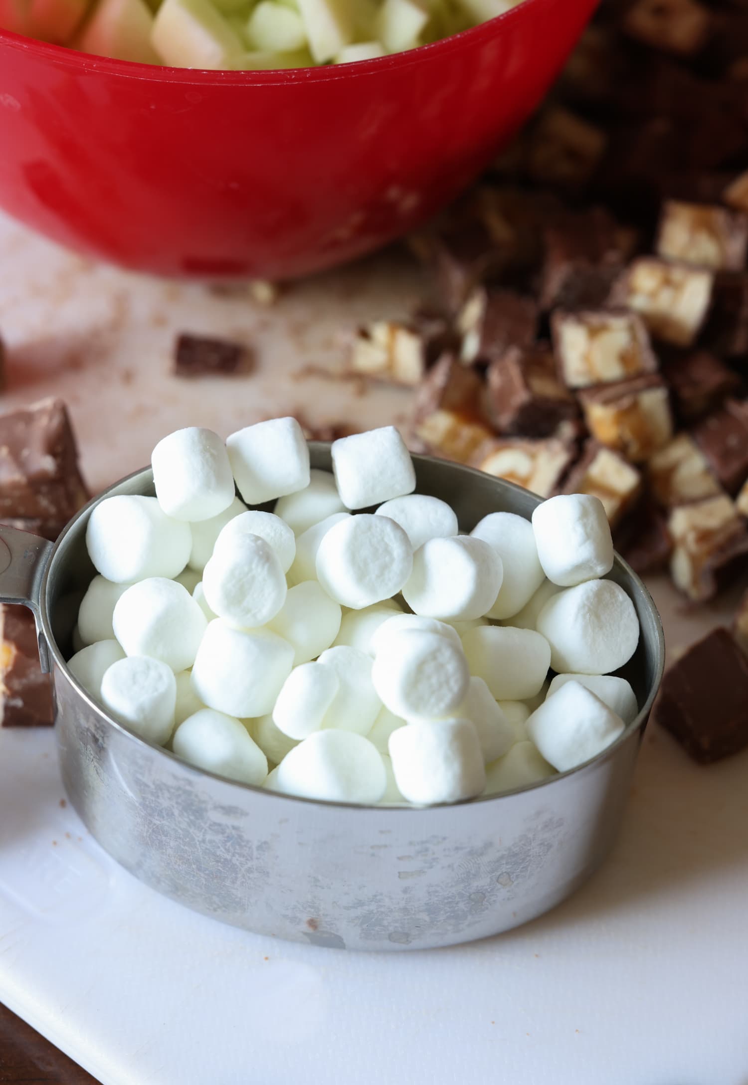 mini malvaviscos en una taza medidora con barras de snickers picadas en una tabla para cortar