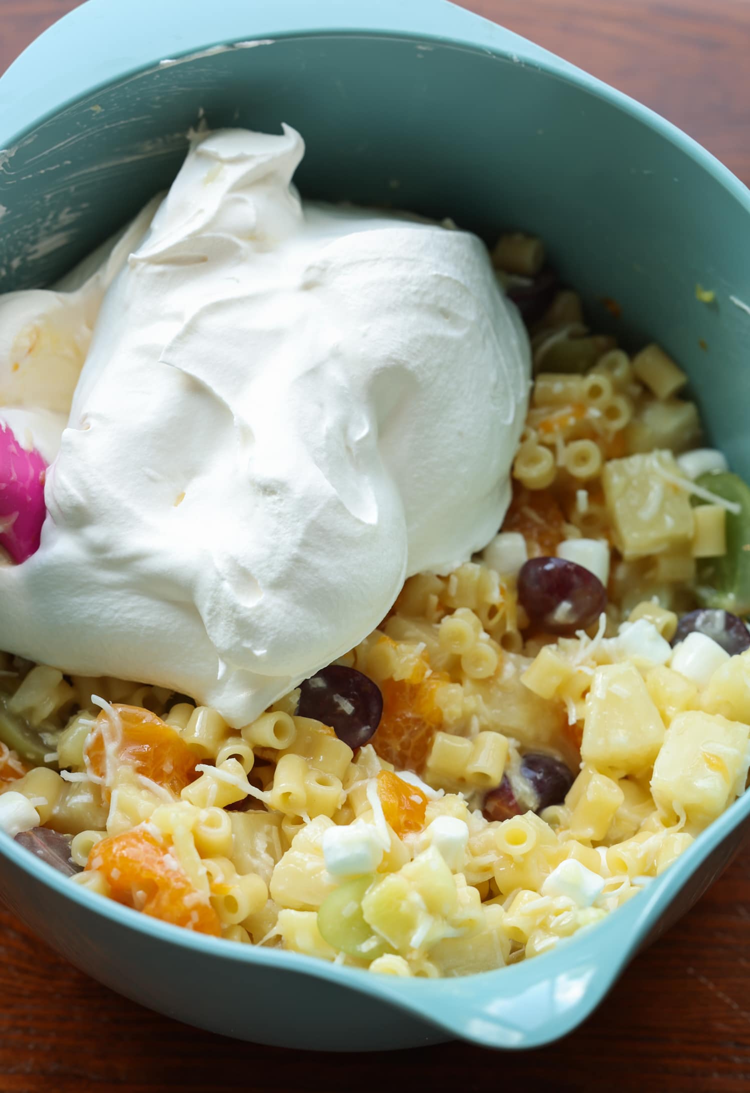 Frog Eye Salad es una ensalada dulce de verano con fruta, natillas, cobertura batida y pasta. ¡Es una delicia de textura y sabor, y es la receta de guarnición perfecta para su barbacoa de verano! un tazón lleno de fruta y pasta, con una cucharada de Cool Whip revolviendo con una espátula de goma
