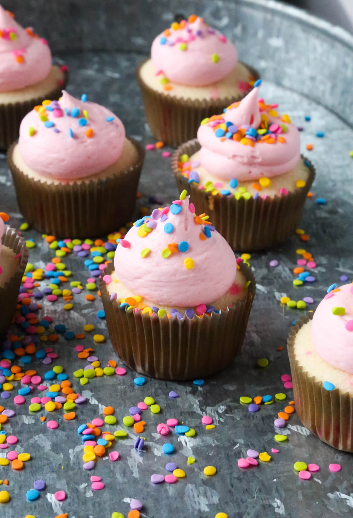 Pastelitos de confeti con glaseado rosa y chispas encima en una bandeja cubierta de chispas