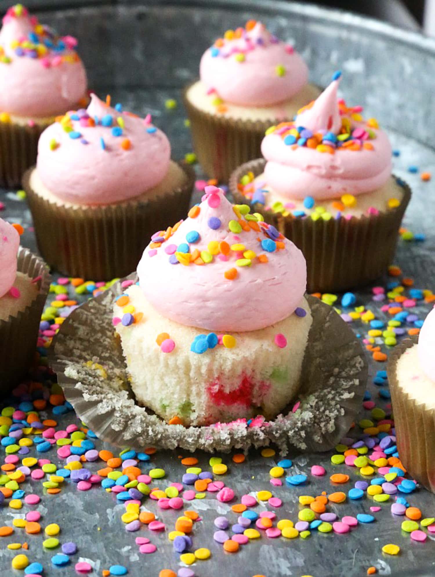 Un cupcake espolvoreado con el forro pelado hacia atrás cubierto con glaseado de crema de mantequilla rosa y chispas