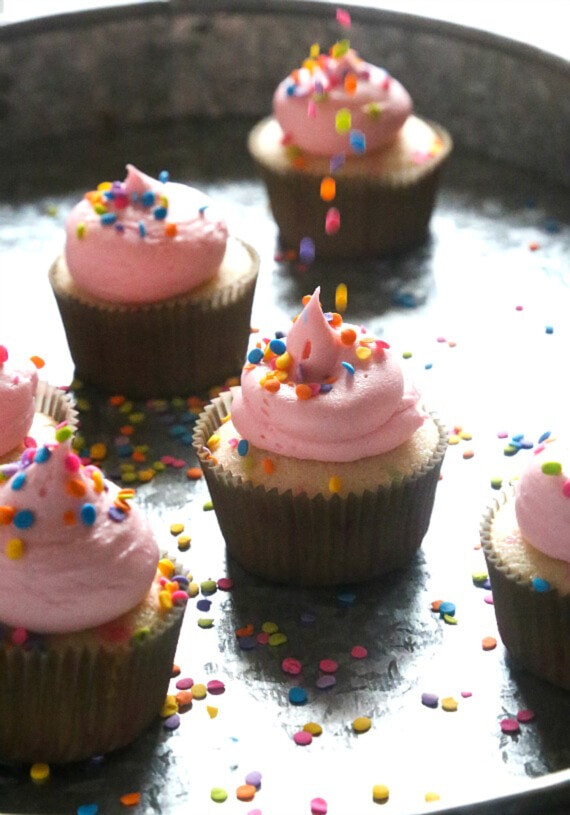 dejando caer chispas de quin en cupcakes de vainilla escarchados de rosa en una bandeja