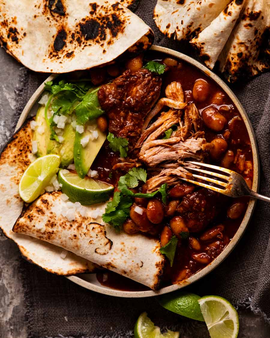 Cerdo con chipotle mexicano y frijoles con tortillas, aguacate y limas al lado