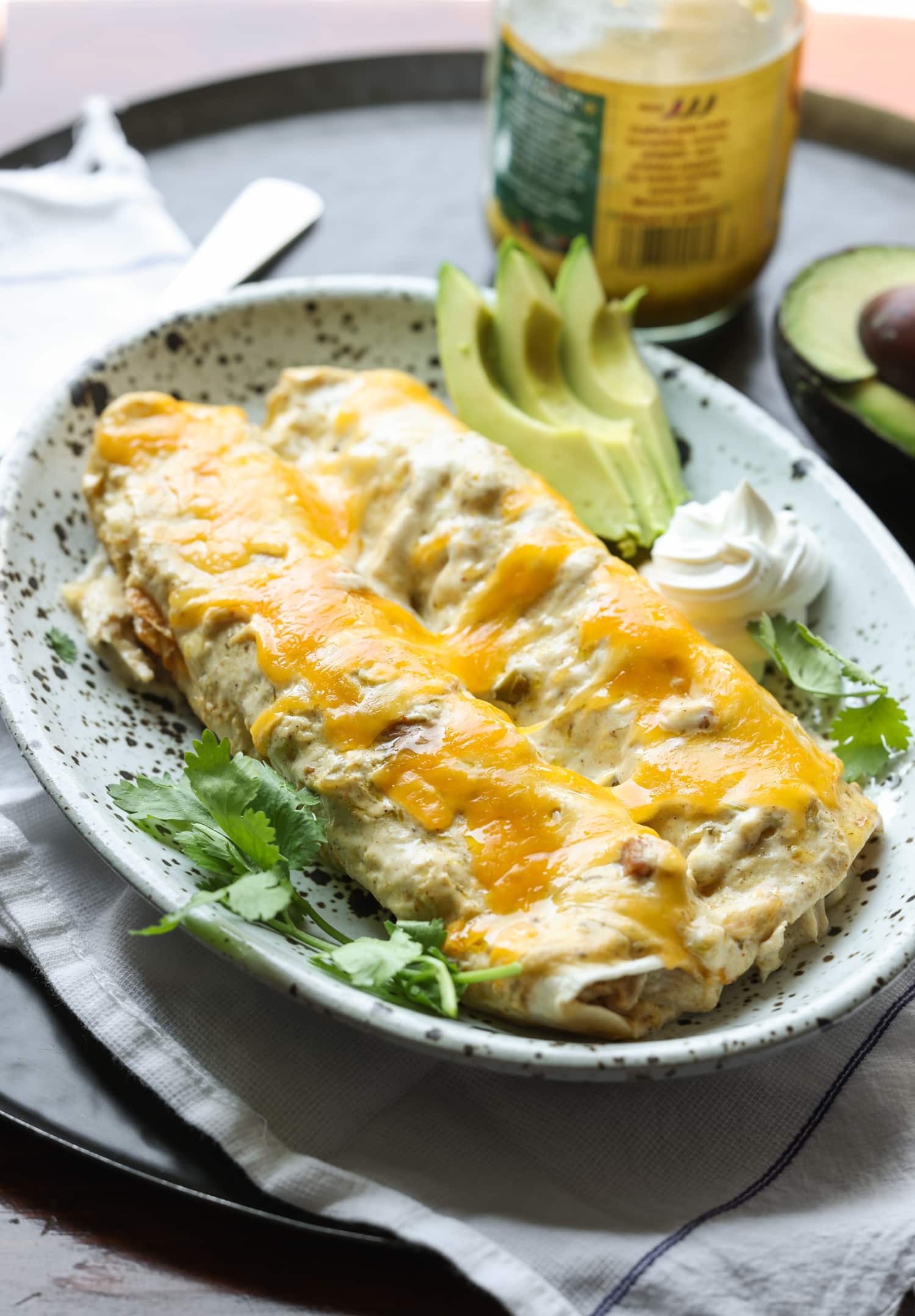 Enchiladas de pollo en un plato cubierto de queso derretido con rodajas de aguacate
