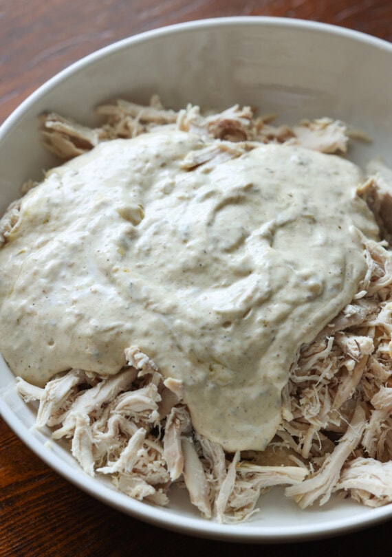 salsa de enchilada de crema agria vertida sobre pollo desmenuzado en un tazón blanco