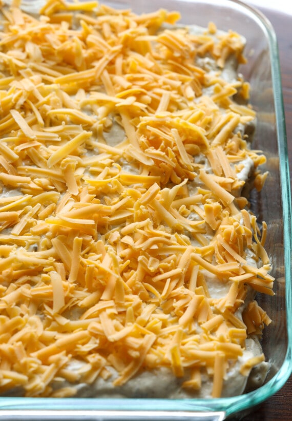 queso rallado encima de enchiladas enrolladas en una cacerola antes de ir al horno
