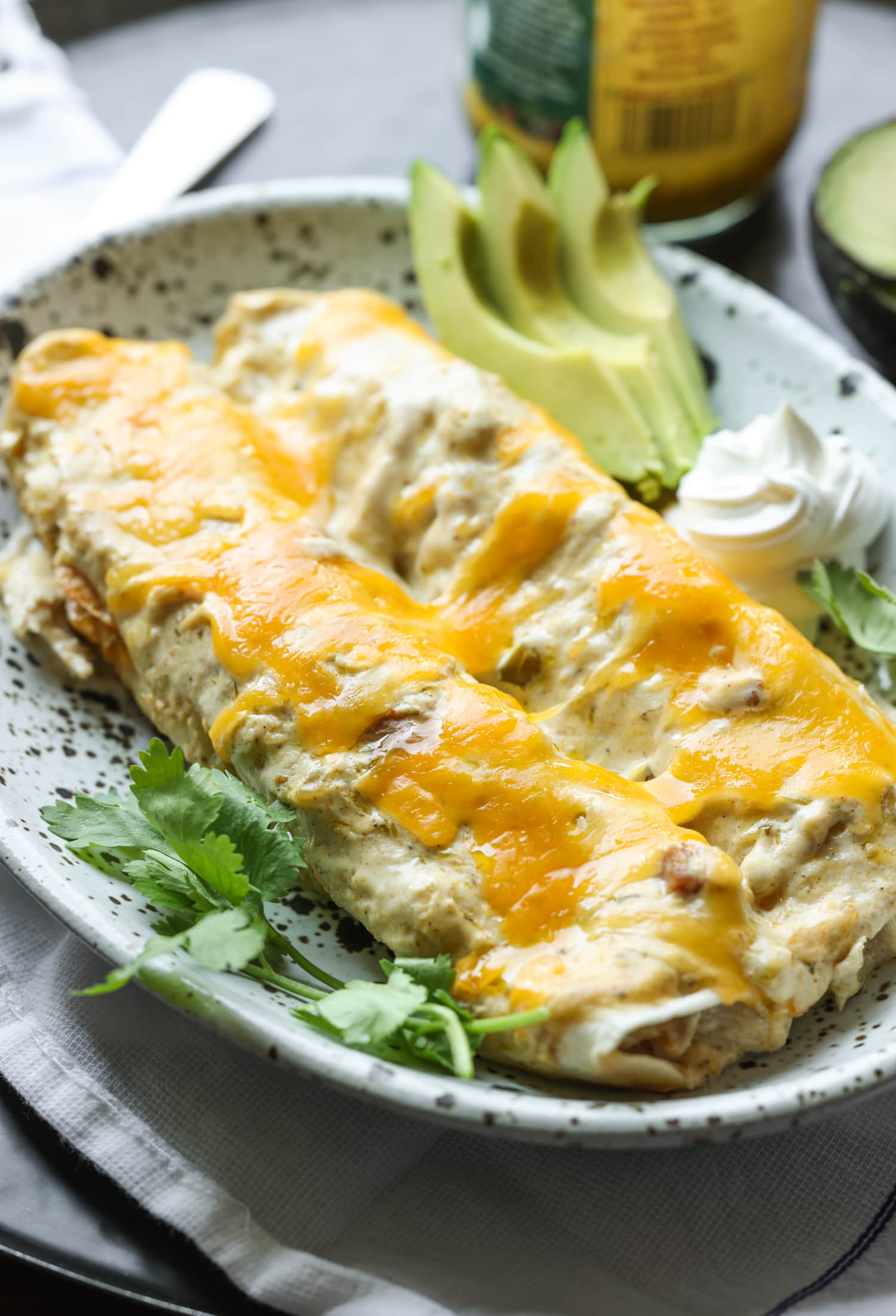 2 enchiladas de pollo en un plato con cilantro, rodajas de aguacate y crema agria